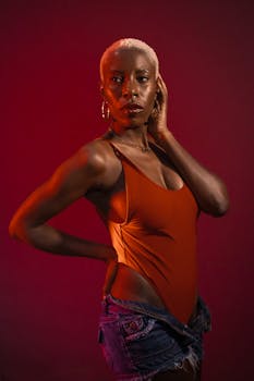 Bold portrait of a woman with short, dyed hair in a striking fashion pose against a red background.