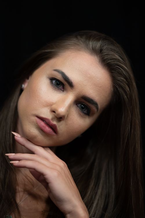 Free Portrait of a woman with hand on chin against a black background, capturing elegance and introspection. Stock Photo