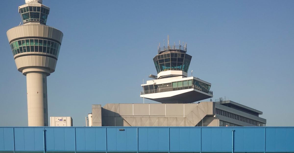 View of air traffic control towers at Amsterdam Schiphol Airport under clear blue sky.