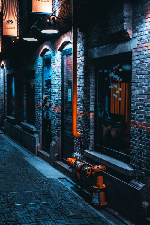 Free Atmospheric nighttime alley with brick buildings, pipes, and soft neon lighting. Stock Photo