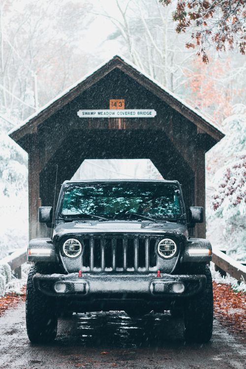 Free A rugged 4x4 vehicle in front of Swamp Meadow Covered Bridge amidst a snow-covered winter scene. Stock Photo
