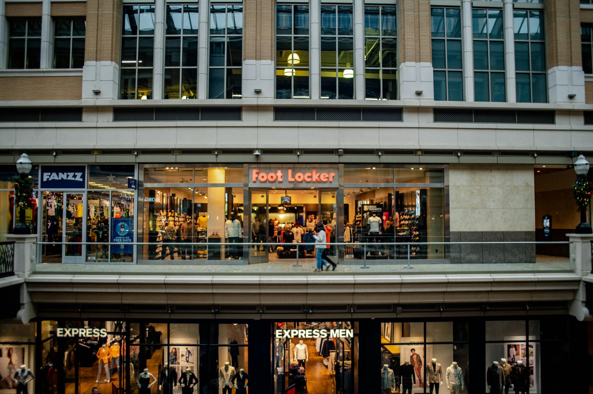 View of a shopping mall interior featuring Foot Locker and Express stores with people walking by.