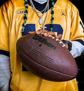 Detailed view of a football player's hand holding a Wilson ball while wearing a yellow jersey and accessories.