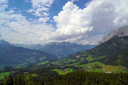 Breathtaking view of a lush green mountain valley under a dramatic cloud-filled blue sky.