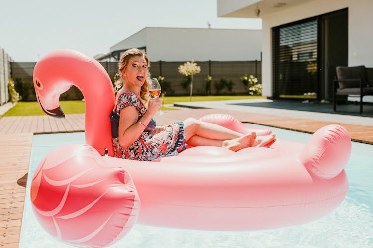 Woman Sitting On Pink Flamingo Floater On Swimming Pool