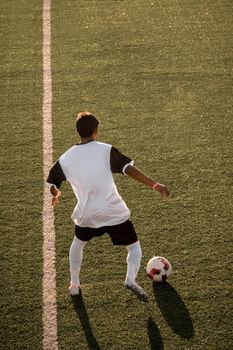 Back view of soccer player in action on a sunlit field, ready to play.