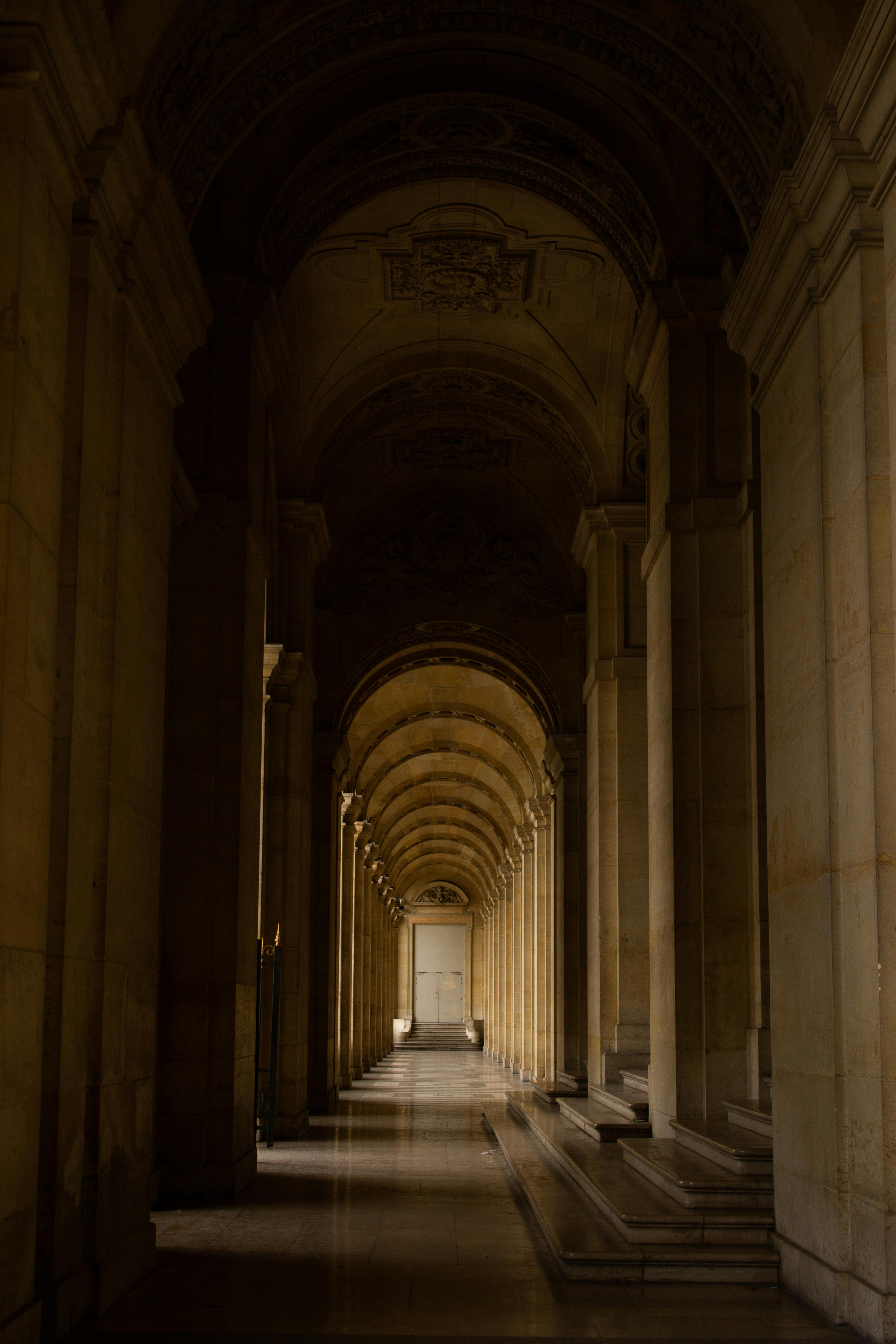 A dimly lit marble corridor with vaulted arches and intricate designs, evoking a historic ambiance.