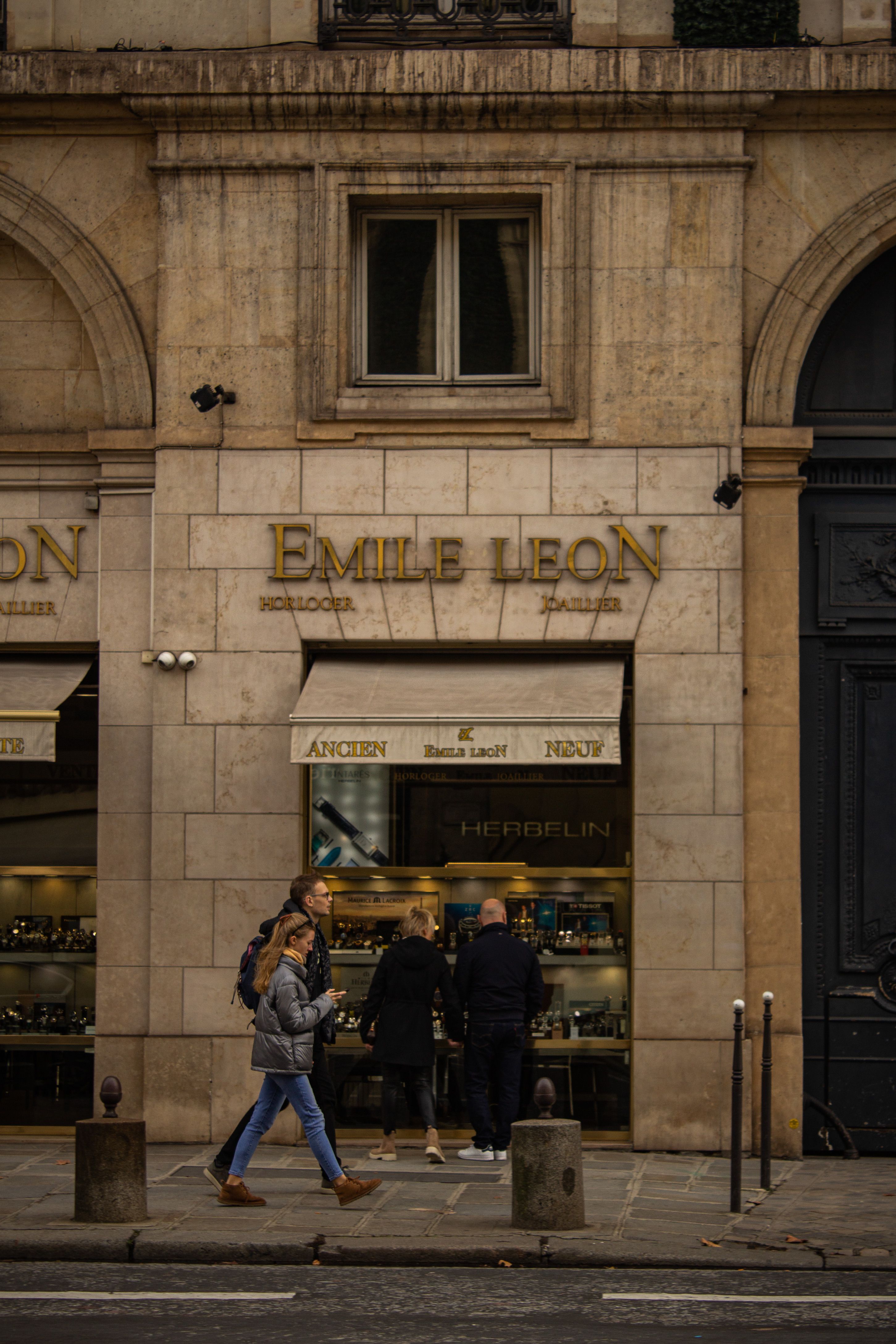 People walking past the Emile Leon store on a city street with an old building facade.