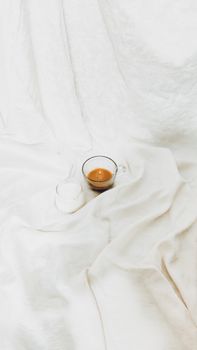 A minimalist scene featuring a glass of espresso and milk on white bedsheets.