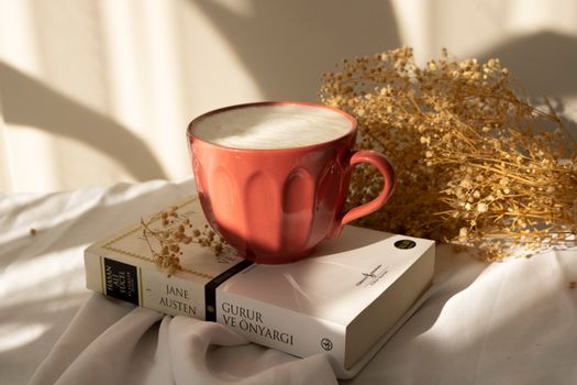 Warm sunlight on a coffee mug with Jane Austen's book and dried flowers. A cozy setup for leisure reading.