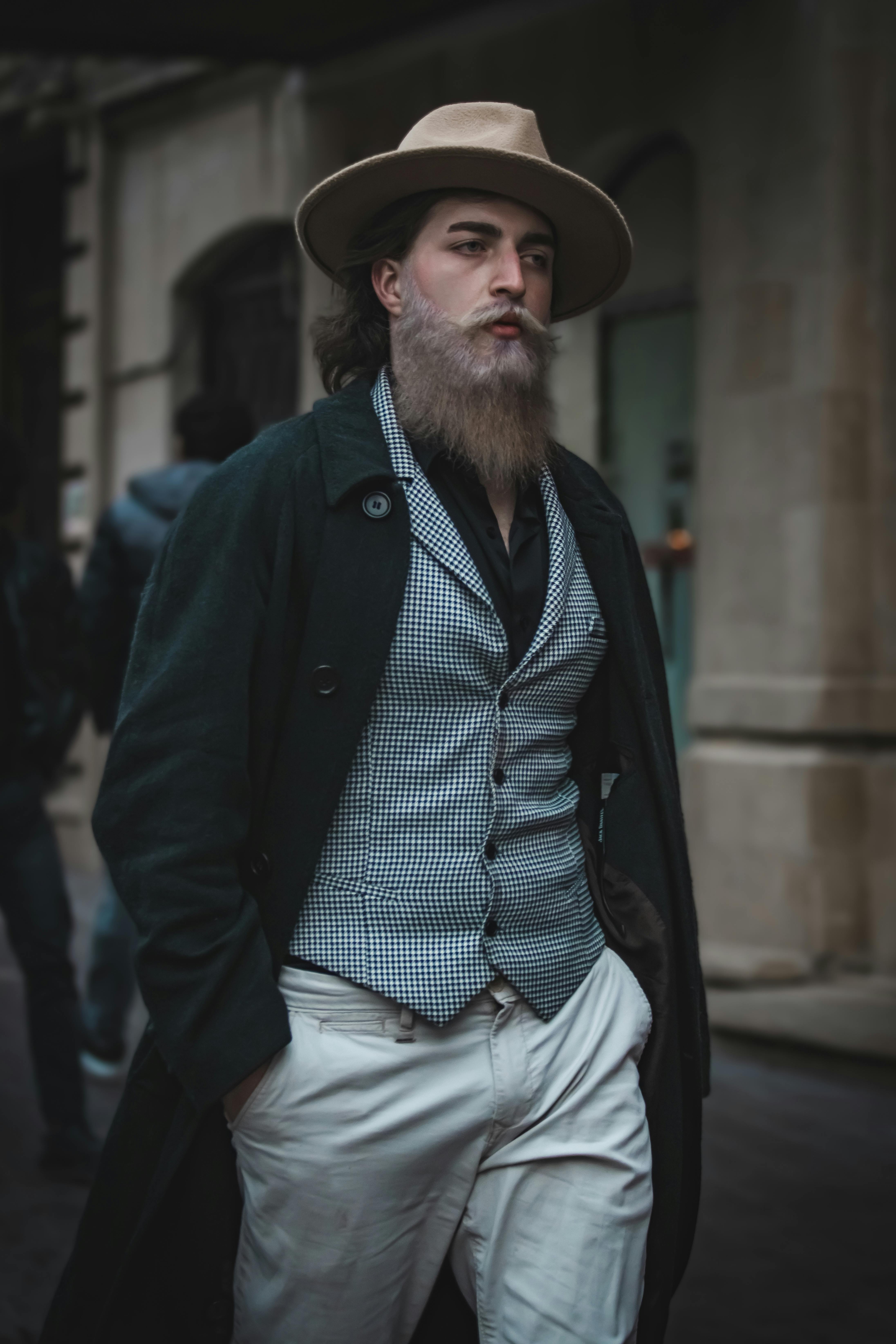 Elegant bearded man in a trench coat and hat strolling through Baku, showcasing street fashion.