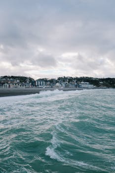 A coastal town with waves splashing against the shore under a cloudy sky.