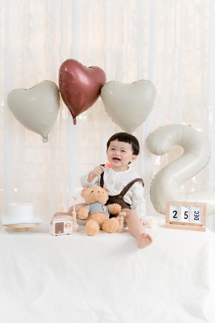 Laughing Boy Sitting With A Teddy Bear At His Birthday Party