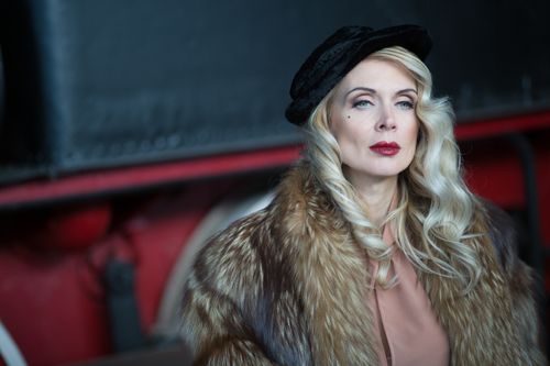 Free Portrait of an elegant woman with blonde hair in a fur coat and black hat, exuding vintage glamour. Stock Photo