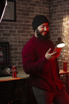 Casual bearded man in a beanie smiling while using a smartphone indoors.