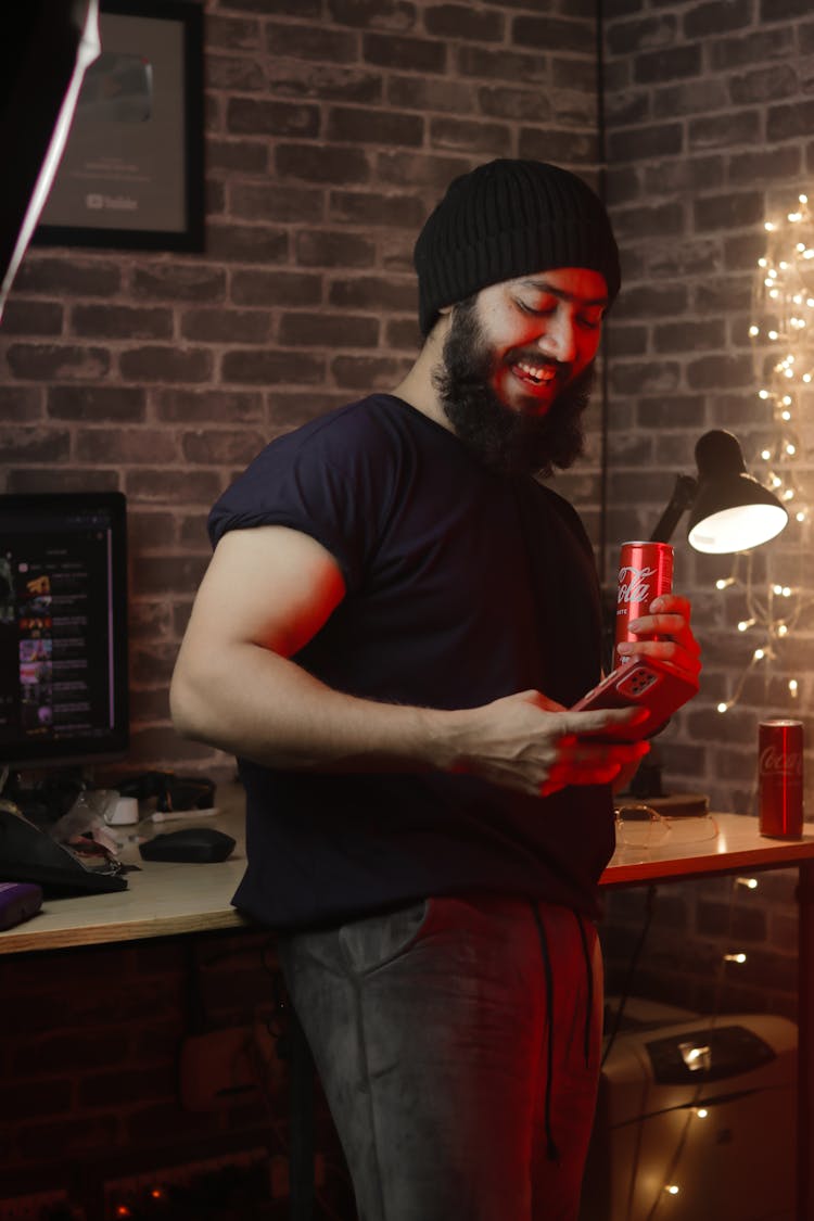 A Man Holding A Smart Phone And A Can