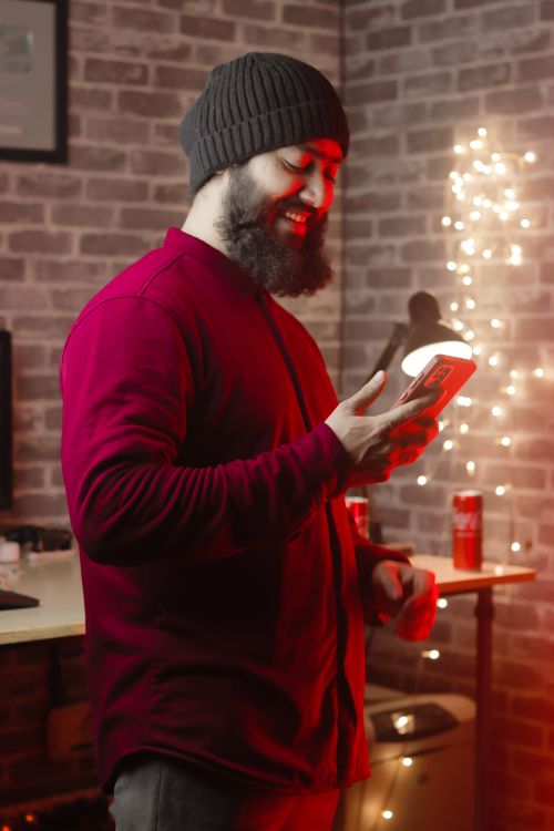 Free A young man is using his smartphone in a stylish, cozy indoor setting decorated with lights. Stock Photo