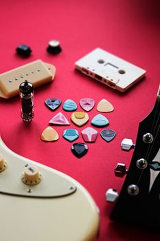 Array of guitar picks and parts on a vibrant red background, featuring electric guitar elements.