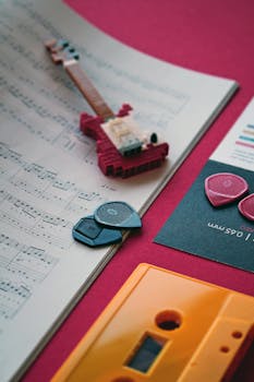 A creative flat lay featuring guitar picks, a miniature guitar, cassette, and music notes on sheet paper.