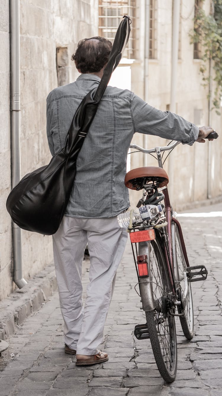 People Rolling A Bicycle With Instrument On His Back