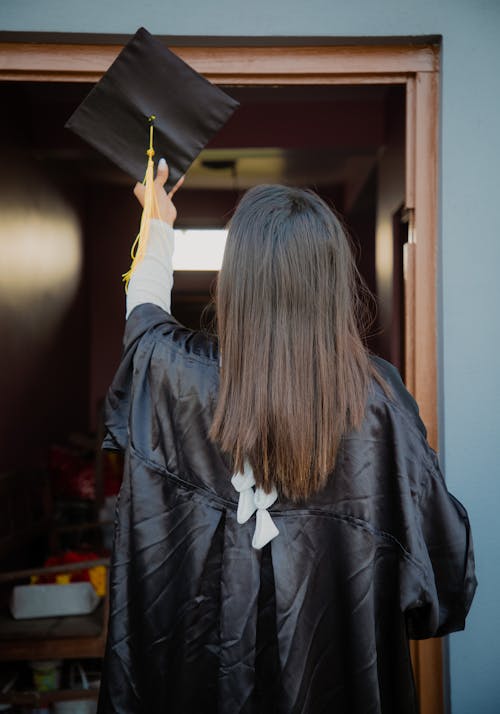 Backview of a Female Graduate in Academic Dress holding a Graduation Cap