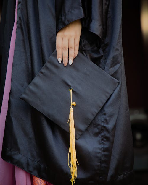 Person in Graduation Gown Holding an Academic  Cap