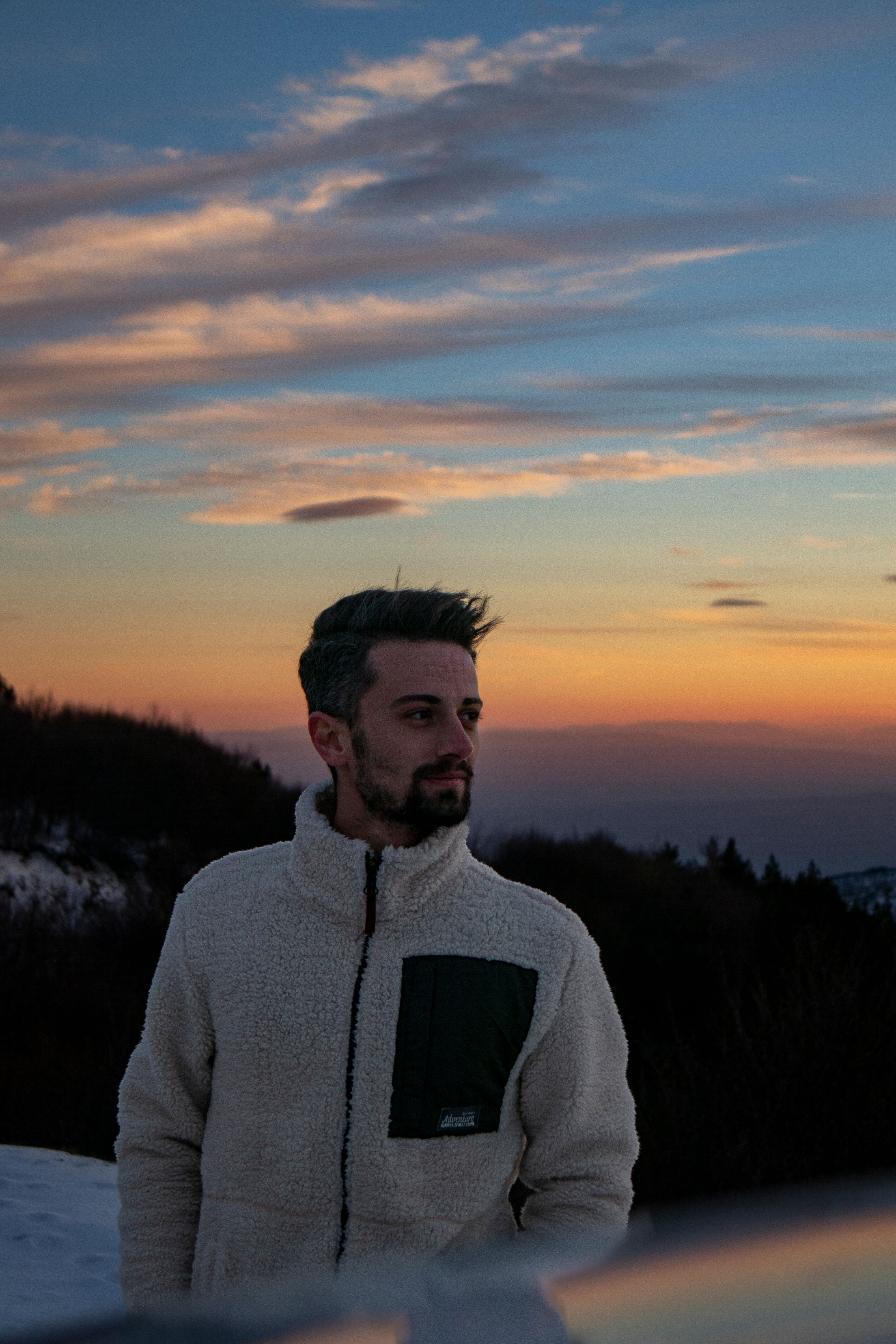 A man in a warm jacket admires a serene winter sunset outdoors.