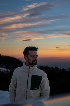 A man in a warm jacket admires a serene winter sunset outdoors.