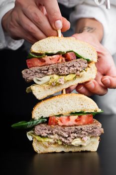 A close-up shot of gourmet burger halves, stacked with fresh ingredients, held by a hand.