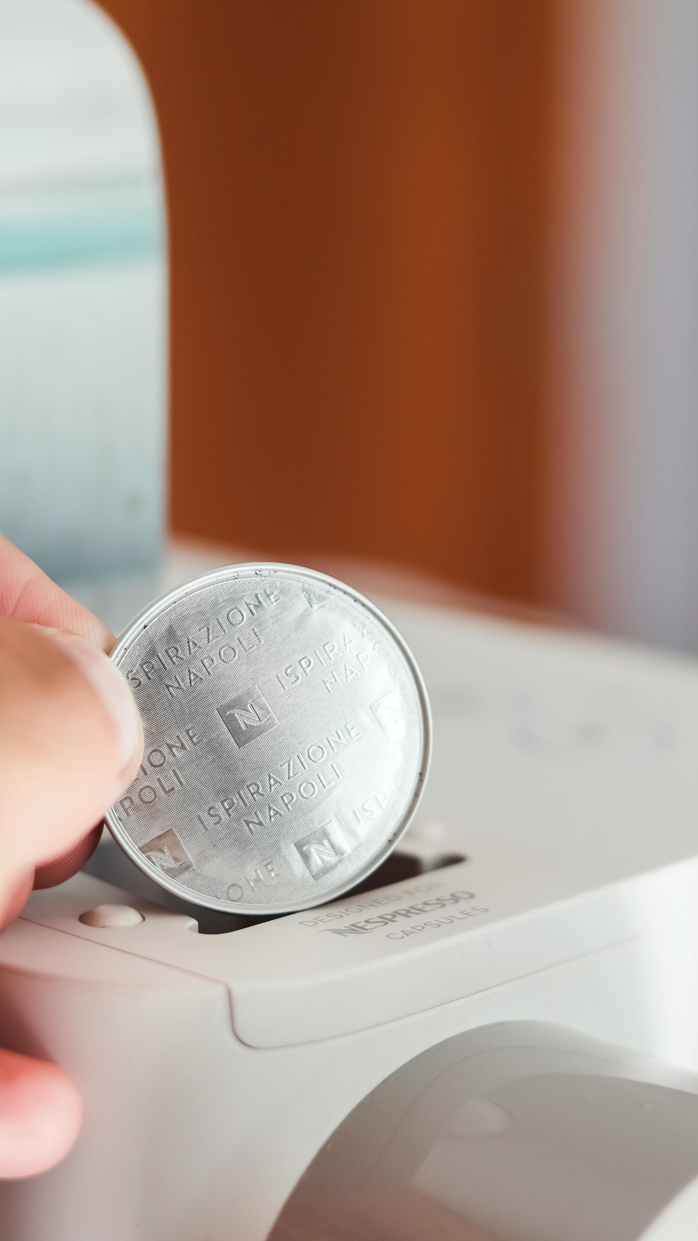 Close-up of hand inserting coffee capsule into a coffee machine for brewing.