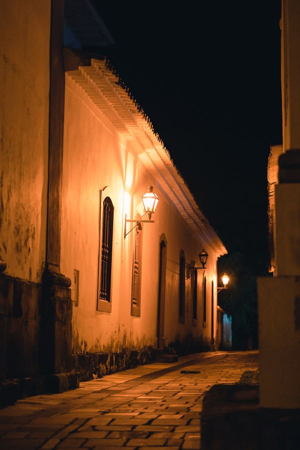 Rua de paralelepípedos iluminada por lampiões quentes em Tiradentes, Brasil, mostrando a arquitetura histórica à noite.