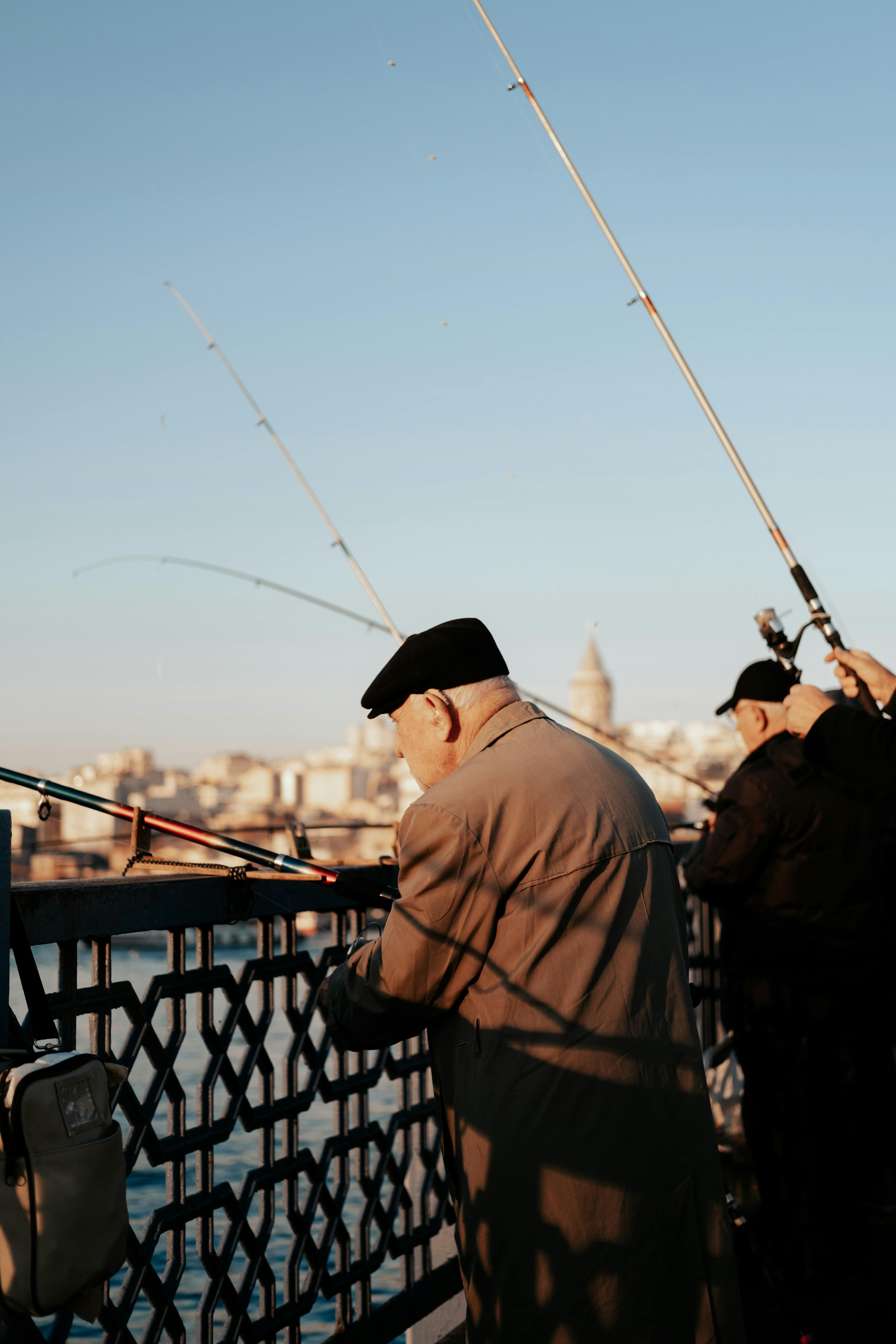 Two senior men fishing on Galata Bridge in Istanbul with a view of the cityscape at sunset.