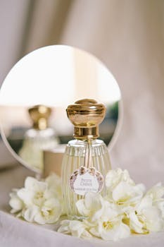 Elegant perfume bottle with floral arrangement and mirror reflection, showcasing luxury.