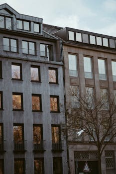 Vertical shot of urban residential building facades in a cityscape with a tree and clear sky.