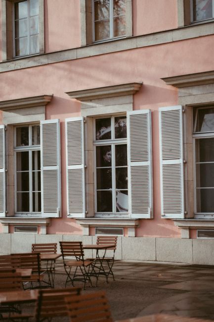 Elegant outdoor cafe setting with pink wall and white shutters, perfect for a relaxed vibe.
