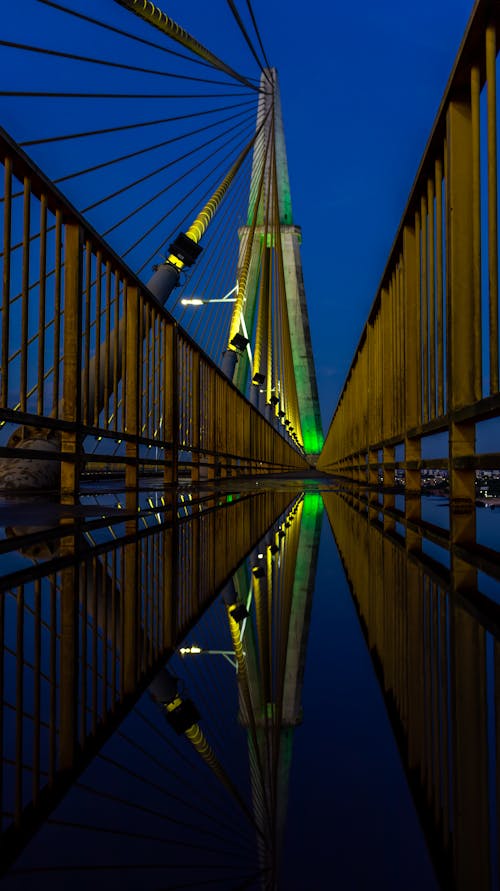A bridge with green and blue lights reflecting in the water
