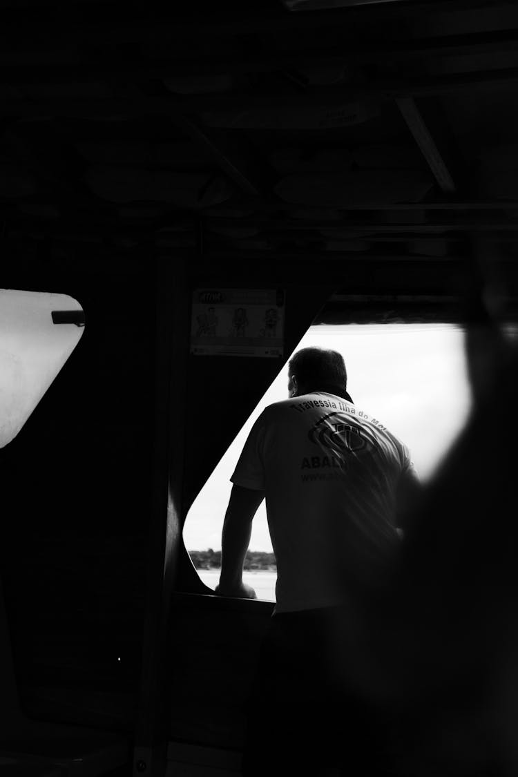 Black And White Shot Of A Man Looking Out Of A Boat Window