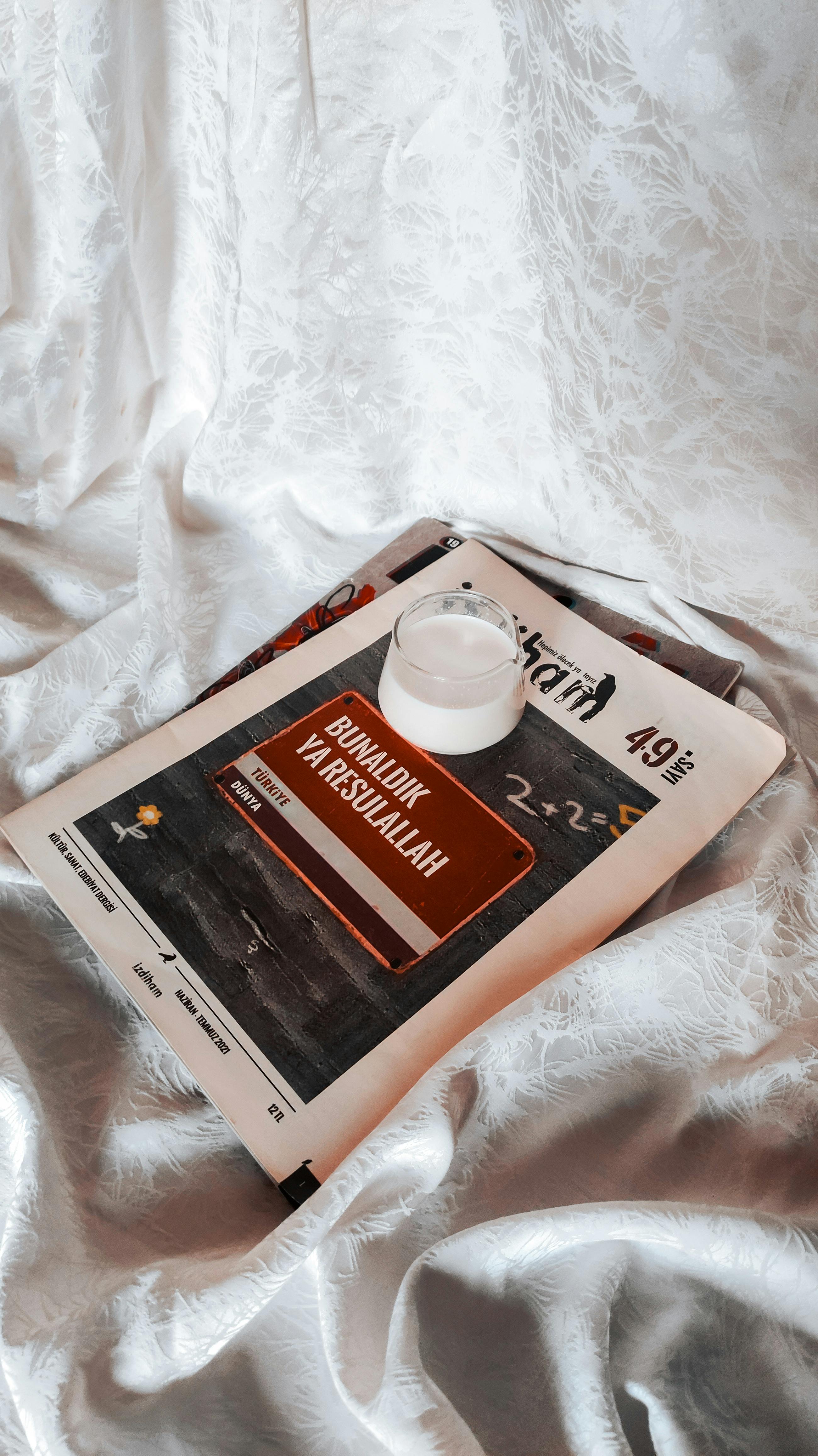 A minimalist composition featuring a drink on a newspaper over white fabric.