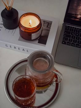 Warm and inviting workspace featuring a lit candle, tea setup, and a laptop.