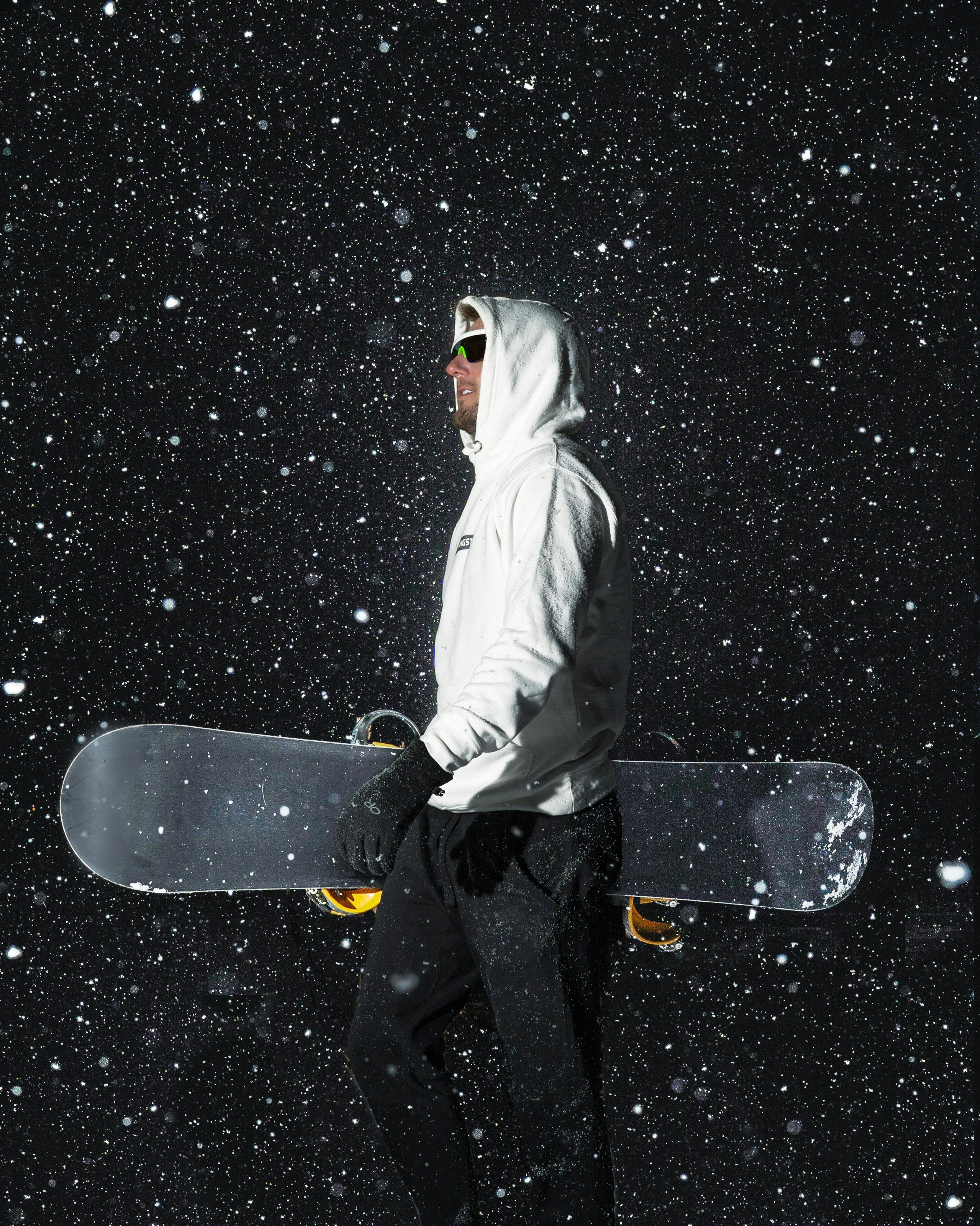 Man in white hoodie with snowboard in snowy Breckenridge night.