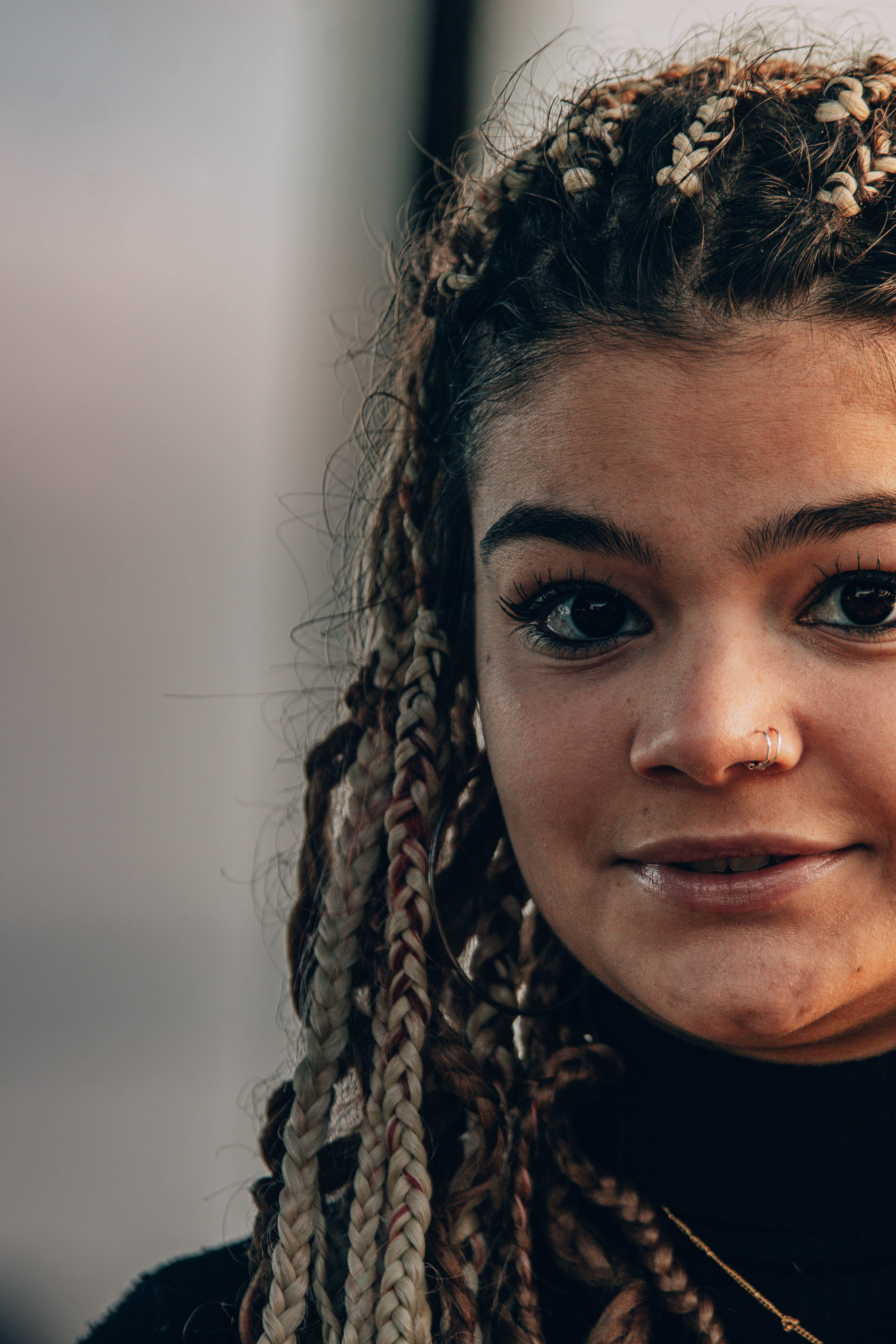 Close-up portrait of a woman with braided hair and nose piercing, exuding a trendy and cool vibe.