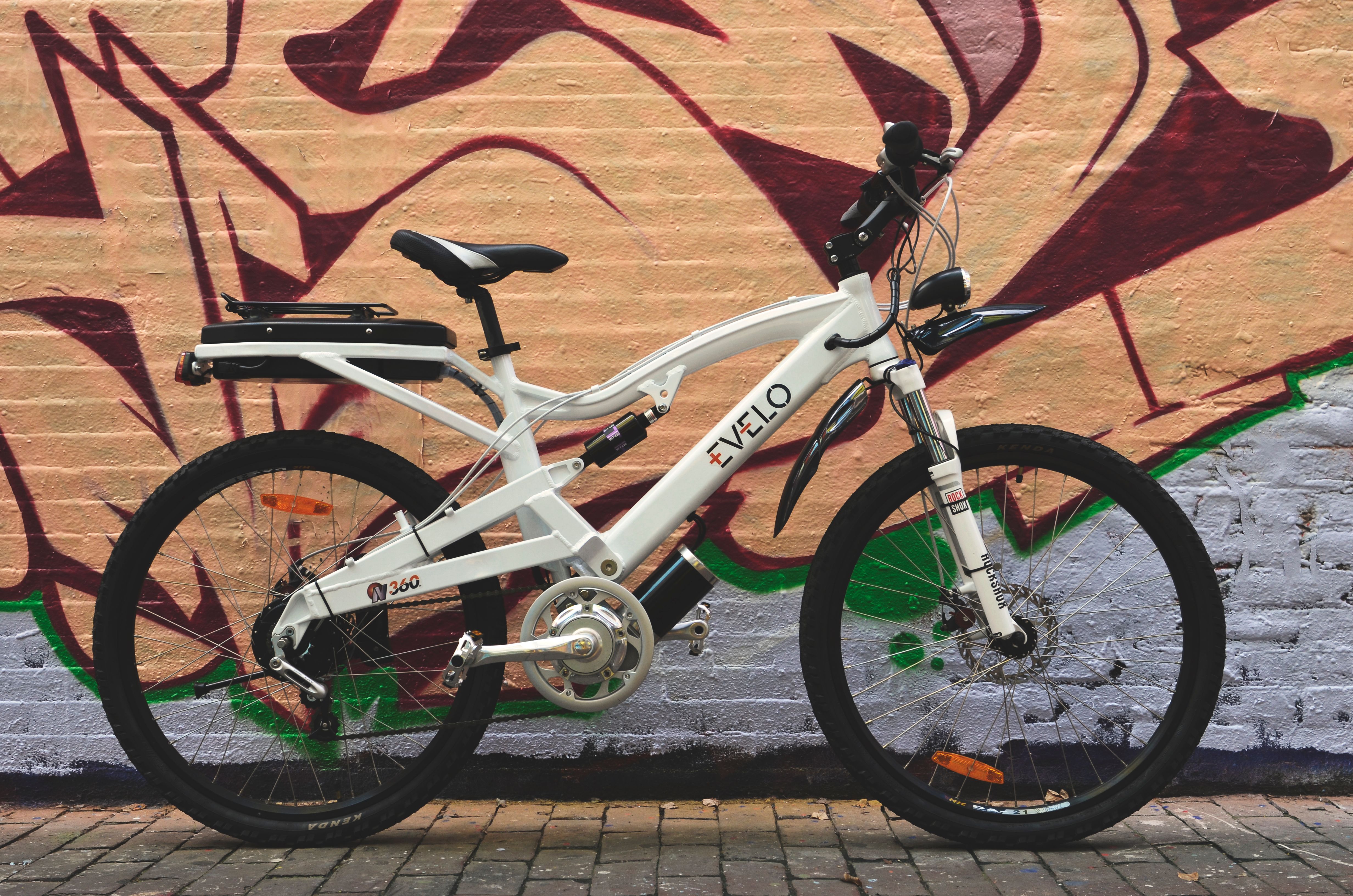 White electric bicycle parked in front of a colorful street art mural.