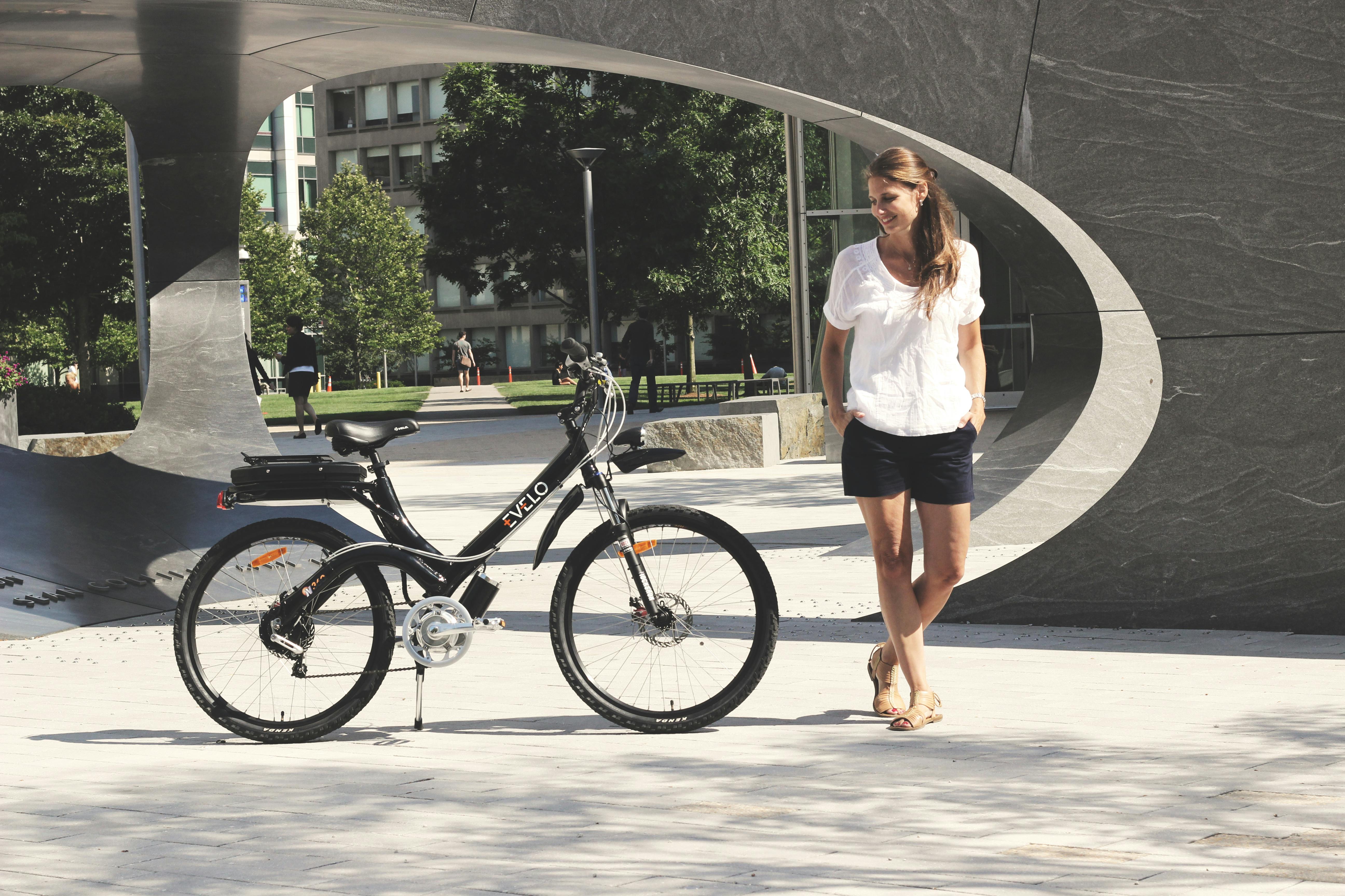 a woman standing next to a bike in front of a sculpture