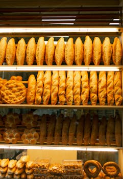 Assorted fresh bread displayed on wooden shelves in a warm-lit bakery.