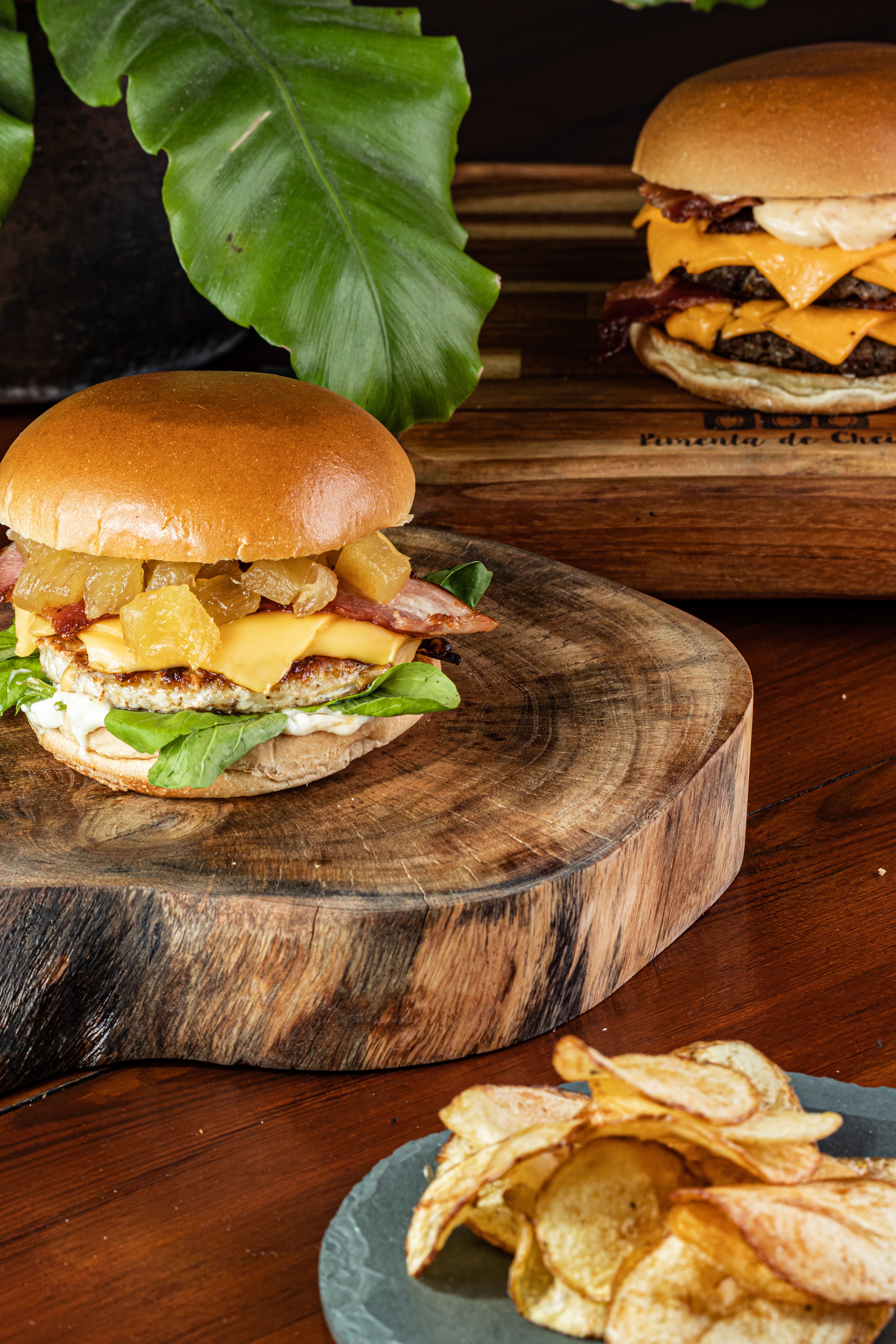 Close-up of gourmet burgers with cheese and chips served on a wooden board.