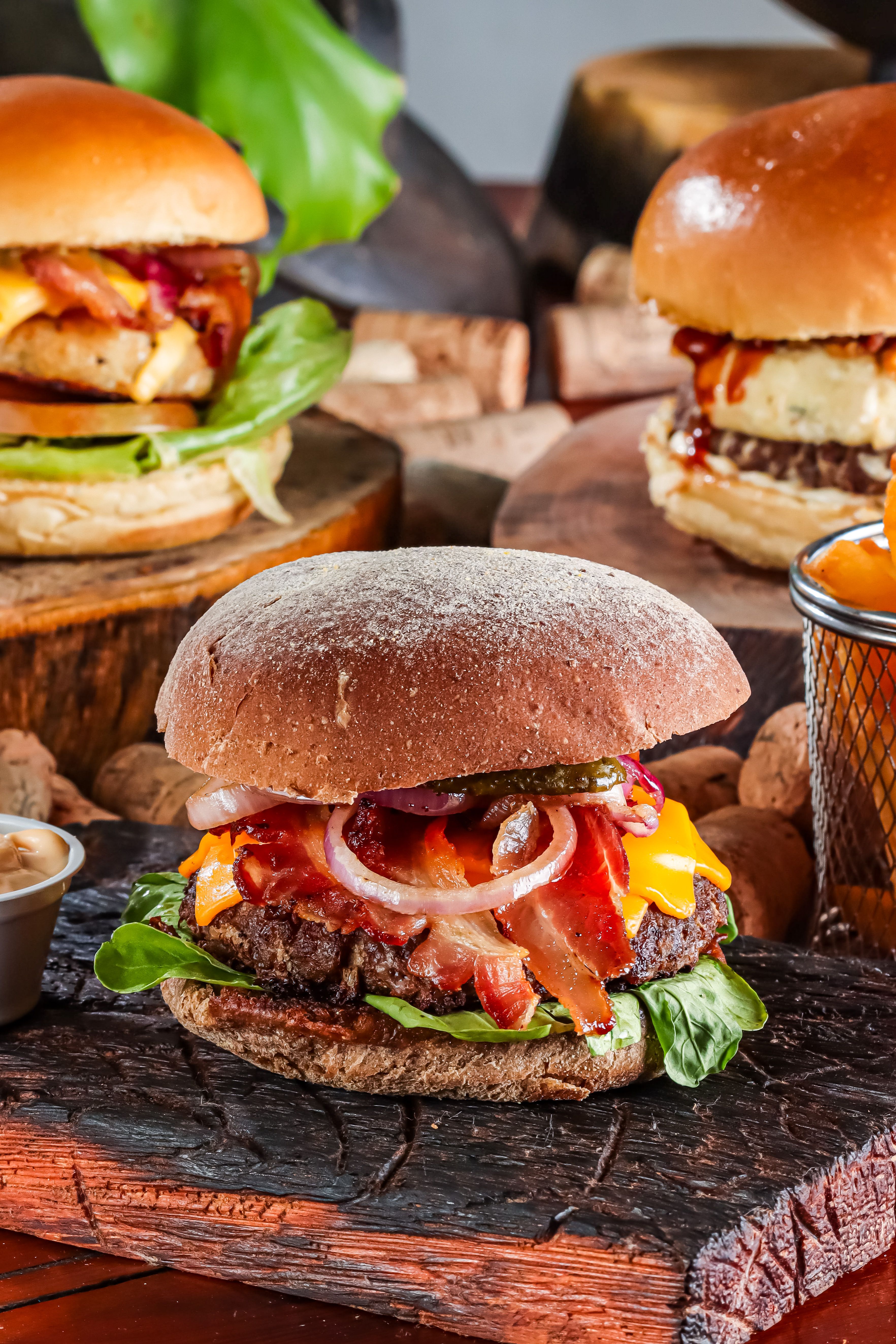 Close-up of gourmet burgers with cheddar, bacon, and vegetables on wooden boards.