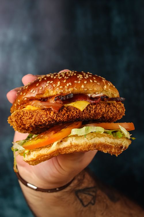 Free Close-up of a hand holding a delicious crispy chicken burger with fresh toppings. Stock Photo