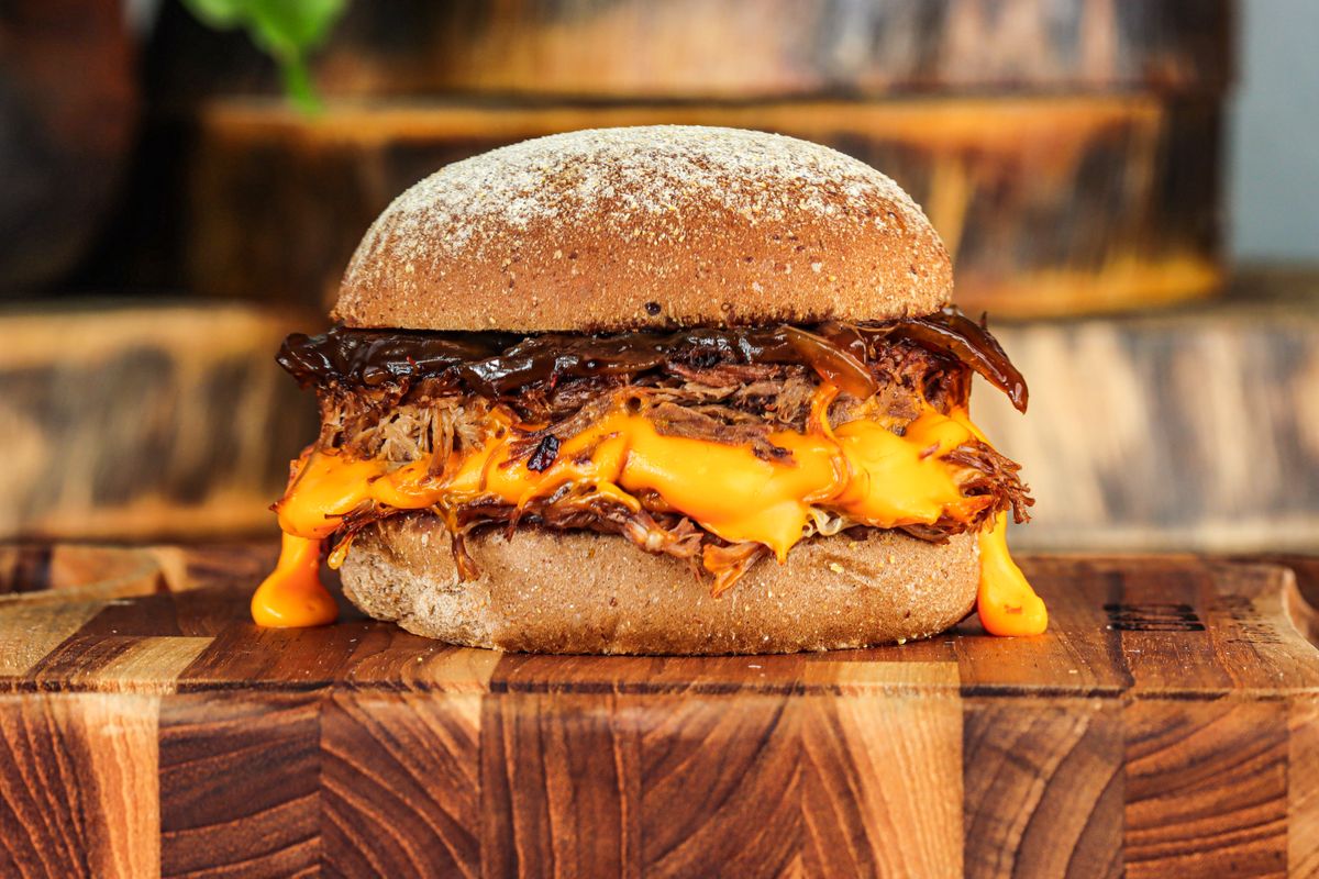 Pulled pork burger with melted cheddar sauce and caramelized onions on a floured bun