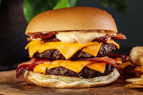 Free Close-up of a mouth-watering bacon cheeseburger with a toasted bun and crispy chips. Stock Photo