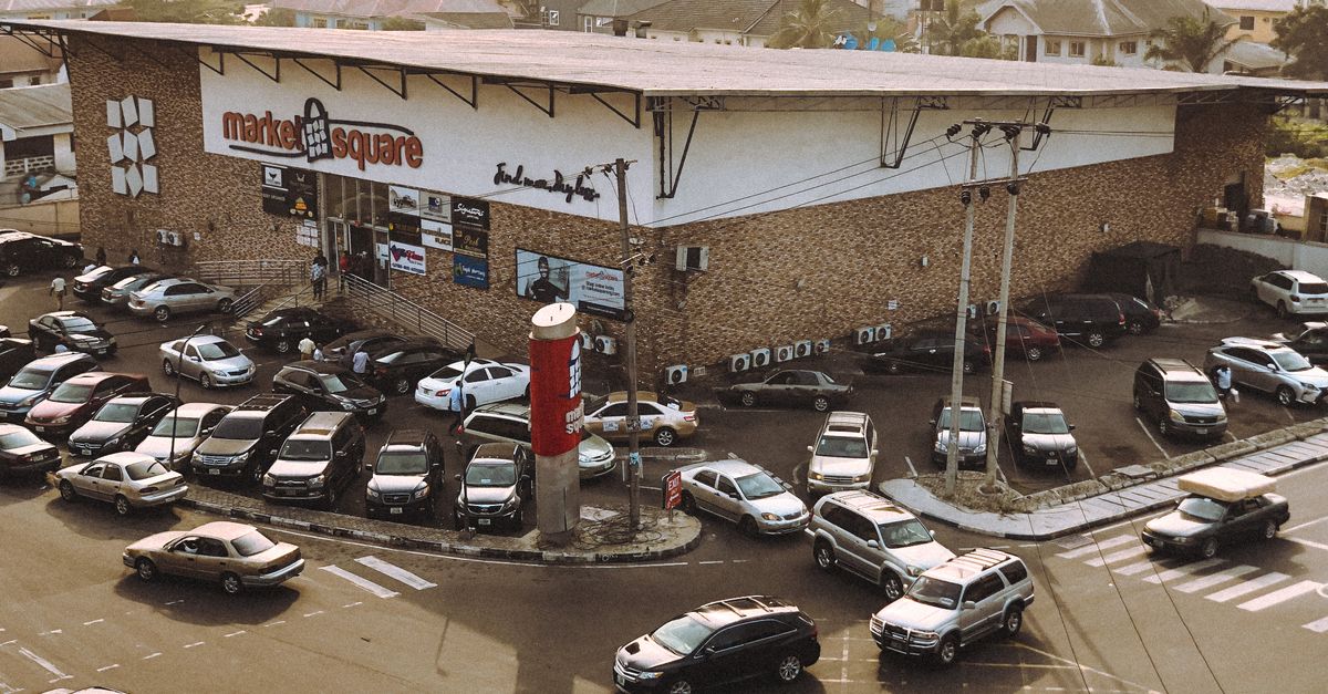 A bustling shopping complex surrounded by parked cars on a busy day.